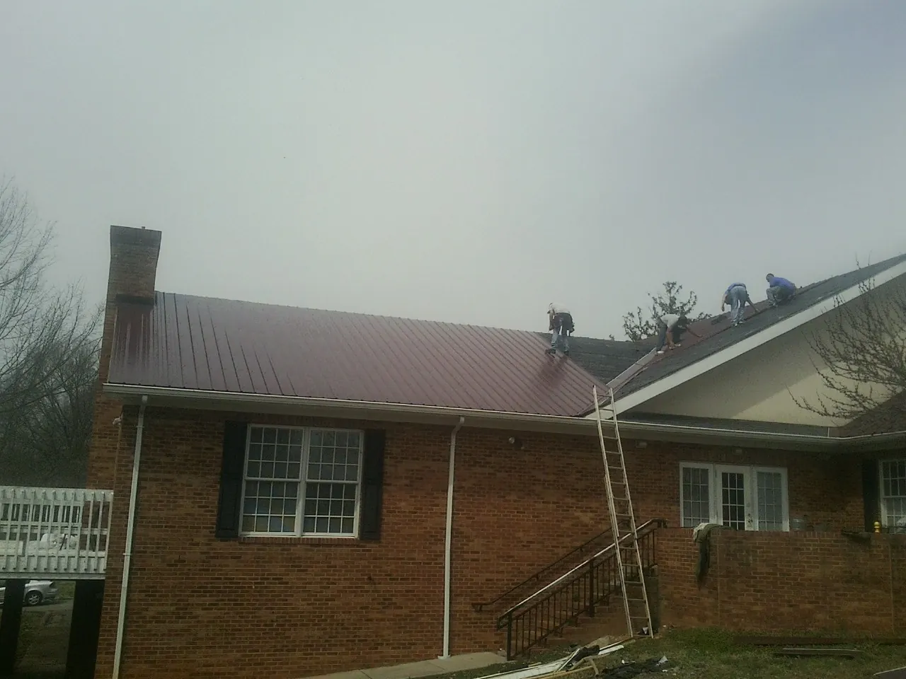 Crew setting red metal roofing panels on a brick home in Naugatuck
