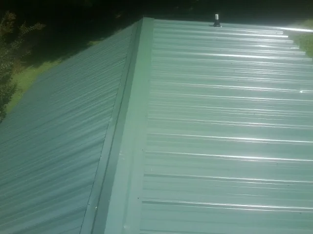 New green metal panels meeting at the ridge of a roof — Flat Roof Repair work by our crew in Naugatuck