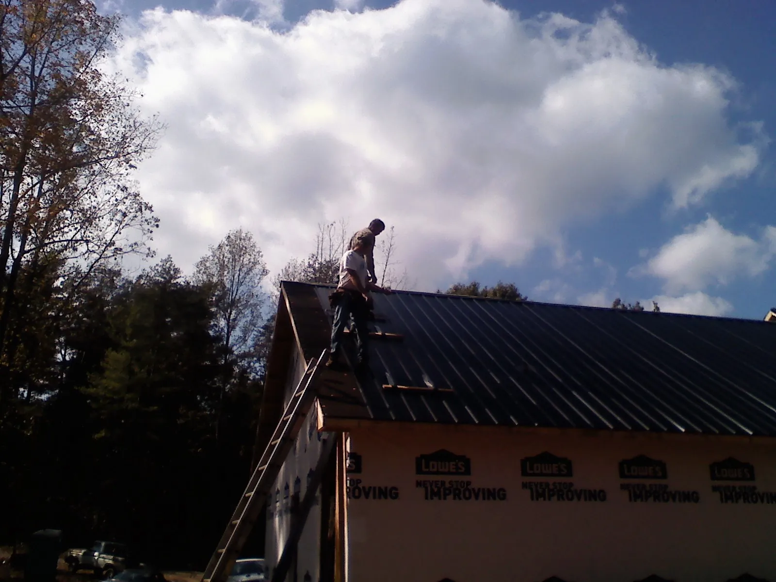 Roofer fastening dark metal panels high against a cloudy sky, from a Roof Inspection job in Naugatuck